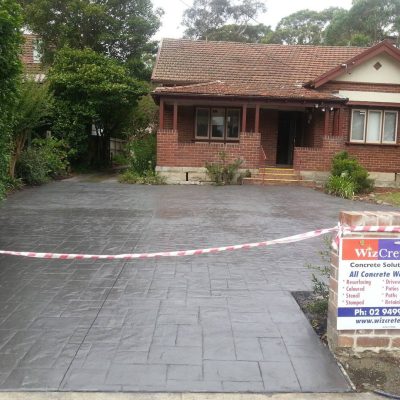 A new stamped concrete driveway in front of a federation home, sectioned off with barrier tape and a Wizcrete signboard on display.